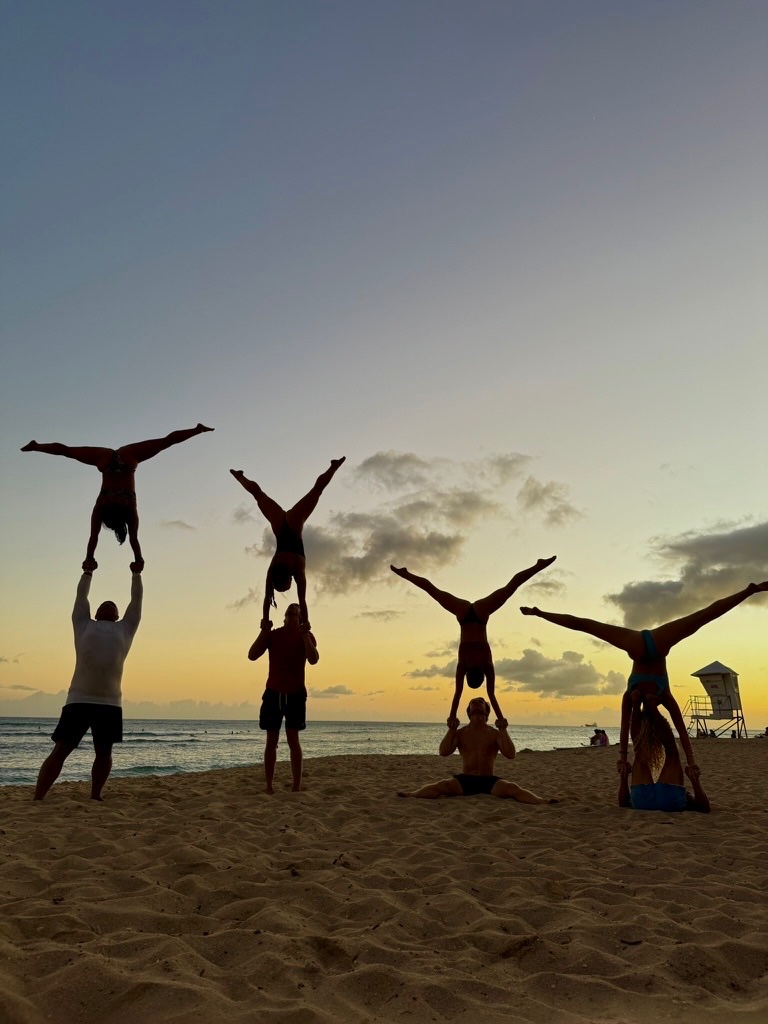 A group of acro partners in handstands and standing acro poses on the beach at sunset